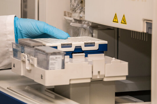 A hand with blue nitril gloves puting a PCR plate into a sanger genetic analyser. Laboratory, DNA analysis, technology, sequencing, equipment, air bubbles, DNA, science, research and development