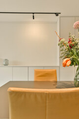 flowers in a vase on top of a table with two orange chairs and a white wall next to the room
