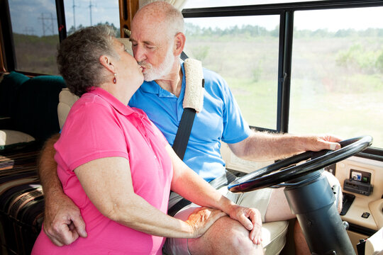 Vacationing senior couple kissing while he is driving their motor home.