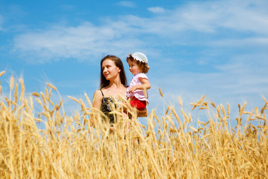 Mother holding daughter in hands, standing in a wheat field