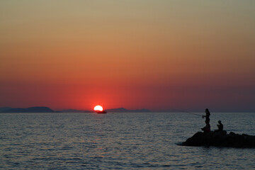 Tourists on holiday in the famous resort town of Bodrum spend time fishing at sunset.