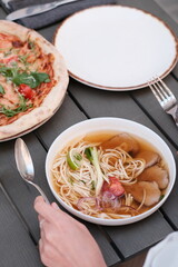 pho broth, Vietnamese soup in a deep plate with meat, wooden Chinese sticks and two quail eggs on a dark background