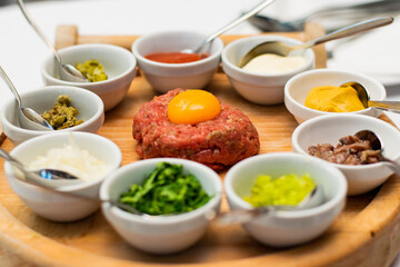 Restaurant waiter serving elaborate  - Beef tartare served on wooden board with various garnishes and egg yolk and person eats it