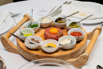 Restaurant waiter serving elaborate  - Beef tartare served on wooden board with various garnishes and egg yolk and person eats it