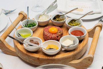 Restaurant waiter serving elaborate  - Beef tartare served on wooden board with various garnishes and egg yolk and person eats it