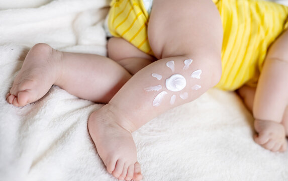 sleeping adorable baby boy on blanket with drawn sun painted from body lotion on leg.mother hand applying cream sun protection sunblock.vacation.fat toddler infant cute feet child in yellow bodysuit