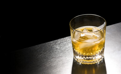 a tumbler with whiskey on ice against a black background