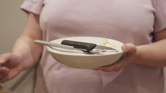 Housewife holds stack of dirty dishes in hands, close-up. Woman puts soiled fork on plate with cutlery. Concept of manual cleaning in the kitchen after eating.