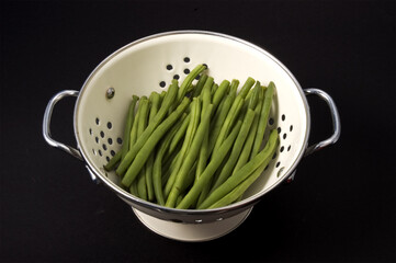 Kitchen collander filled with green beans brightly lit on isolated white background