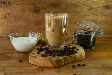 Iced coffee in a glass with milk and coffee beans on wooden background