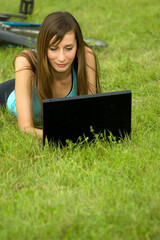 female student with laptop relaxing on the grass