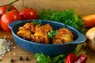 Cabbage rolls with meat and vegetables in a blue bowl on a wooden table