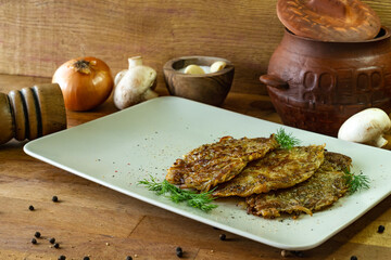 Fried potato pancakes with mushrooms on a white plate on a wooden background