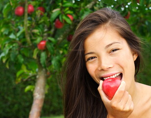 Apple woman. Very beautiful ethnic model eating red apple in the park.