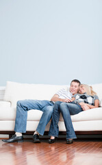 Fototapeta na wymiar Full length view of affectionate couple laughing and relaxing together on white couch. Vertical format.