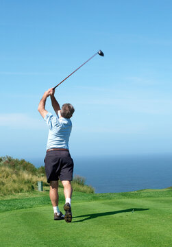 Senior male golfer playing golf from the tee box on a beautiful summer day next to the ocean