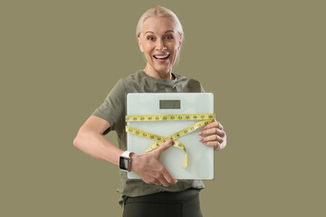 Sporty mature woman with scales and tape measure on green background