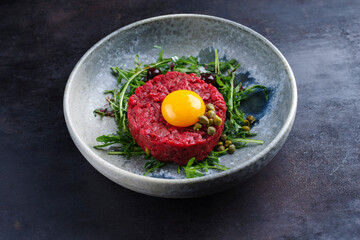 Gourmet Tartar roh aus Rinderfilet mit Ei, Rucola und Kapern serviert als close-up auf einem Design Teller mit Textfreiraum