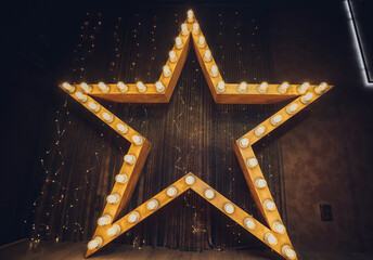 Photo of golden star with light bulbs on red velvet curtain on stage.
