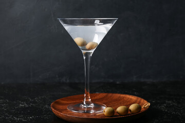Glass of tasty martini and olives on dark background