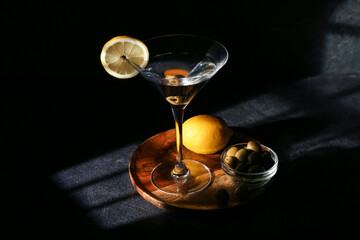 Glass of tasty martini, lemon and green olives on dark background