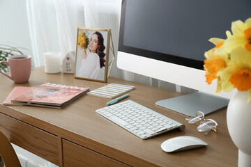 Comfortable workplace with modern PC and narcissus flowers near window