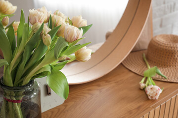 Stylish mirror and tulip flowers on wooden cabinet near white brick wall