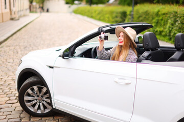 leisure, road trip, travel concept - happy girl driving in cabriolet car and taking picture by film...