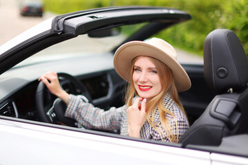 Portrait of Young blond girl in a hat driving cabriolet