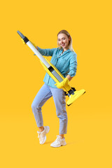 Young woman with vacuum cleaner on yellow background