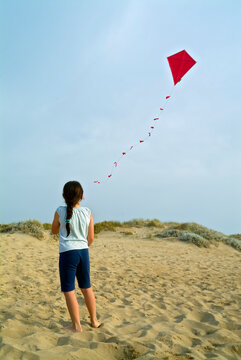 girl on beach playing with a red kite