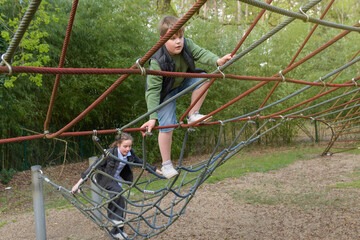 Teenage boy and girl climbing on spider web with expression in public park. Spring sunny day