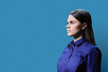 Profile view, portrait of serious young woman on blue background, copy space