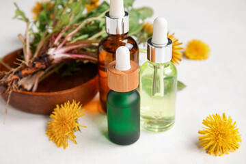 Bottles with cosmetic oil and plate of dandelion flowers on white background