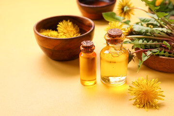 Bottles with cosmetic oil and bowls of dandelion flowers on yellow background