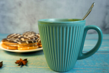 Fototapeta na wymiar turquoise texture mug with a small metal spoon on the background of a plate with chocolate cookies on a blue wooden table. side view . tea breakfast