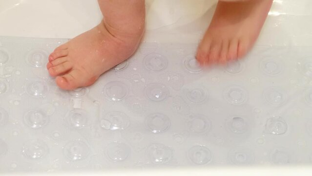 Baby legs is standing on a non-slip mat in the bathtub. Child boy foots washes on the anti slip carpet in the bathroom. Kid about two years old (one year ten months).