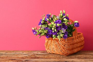 Basket with eustoma flowers on wooden table near red wall