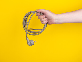 A coiled power cable is held by one hand. Yellow background, no face. Concept. 
