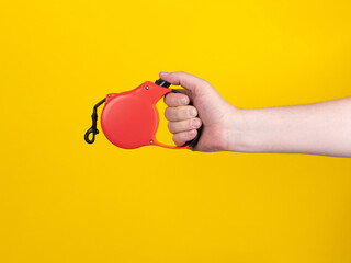 Fototapeta premium Hand pressing button on red dog leash, yellow background. 