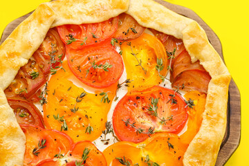 Board with tasty tomato galette on yellow background