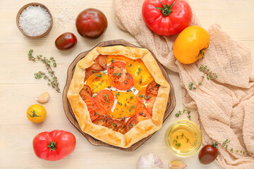 Board with tasty tomato galette on white wooden background