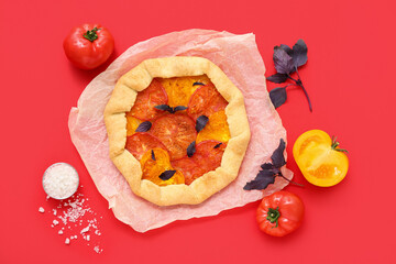 Baking paper with tasty tomato galette and basil on red background