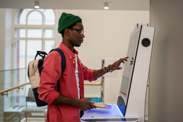 Student African man using self-service electronic terminal to pay for goods in store without...