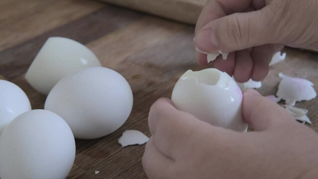closeup of female hands peel white boiled eggs from shell, chicken eggs on wooden table, valuable food product, Easter culinary traditions, cooking at home, protein meals