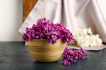 Wooden bowl of beautiful fragrant lilac flowers on black table