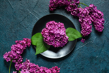 Plate of beautiful fragrant lilac flowers on dark blue grunge background