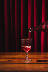 Lambrusco bottle pouring into glass, background of red velvet curtains and wooden table
