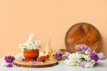Mortar with beautiful lilac flowers on white table near orange wall