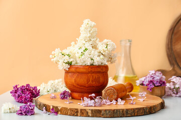 Mortar with beautiful lilac flowers on white table near orange wall